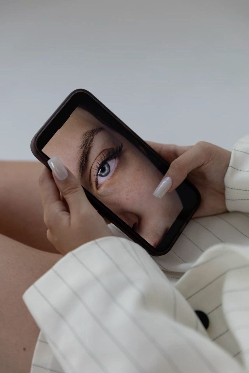 Pose d'extensions de cils par une lash tech avec les produits Maison Moon. Une cliente regarde sur son téléphone une pose de cils professionnelle